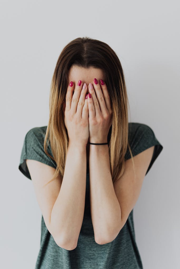 A young woman covers her face with her hands in an expression of fear and anxiety about difficult conversations.